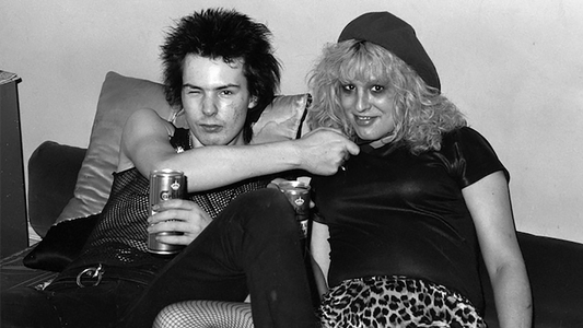 Sid Vicious et Nancy Spungen assis sur un canapé, image emblématique du punk londonien des années 1970 | Sid Vicious and Nancy Spungen sitting on a couch, iconic image of 1970s London punk culture