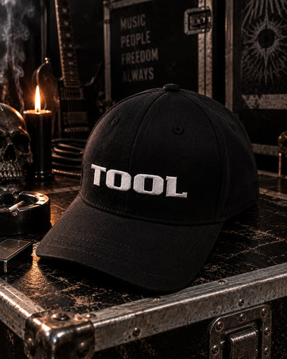 Casquette Tool noire avec logo blanc dans un décor backstage sombre | Black Tool cap with white logo in a dark backstage setting